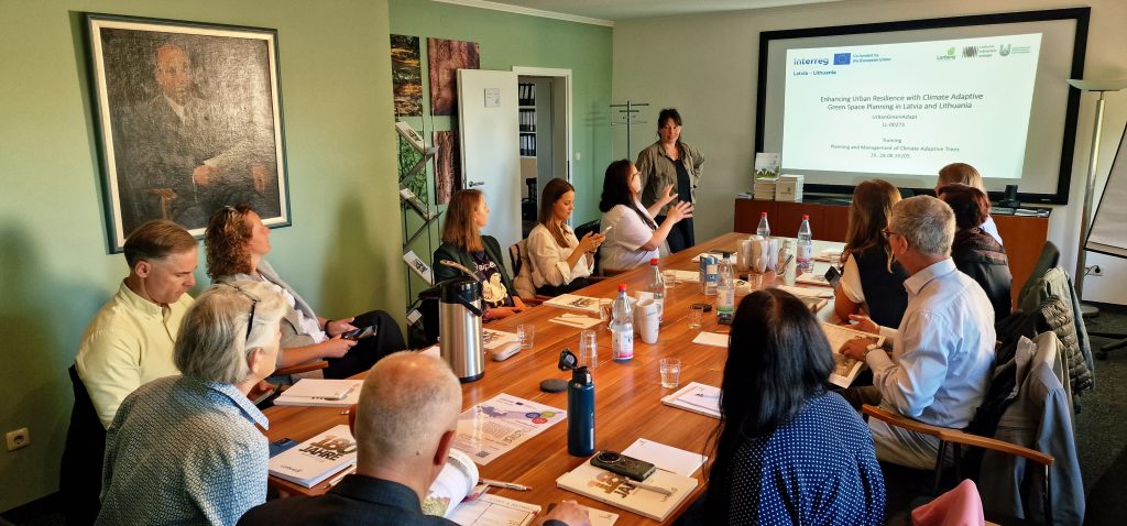 Business meeting in a conference room with participants engaged in discussion, presentation displayed on screen, and various materials on the table.