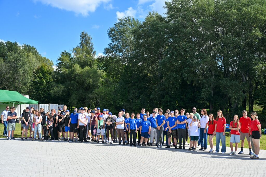 A large group of diverse individuals standing together outdoors, wearing colorful t-shirts, with trees and a blue sky in the background, indicating a community event or gathering. A large group of diverse individuals standing together outdoors, wearing colorful t-shirts, with trees and a blue sky in the background, indicating a community event or gathering.