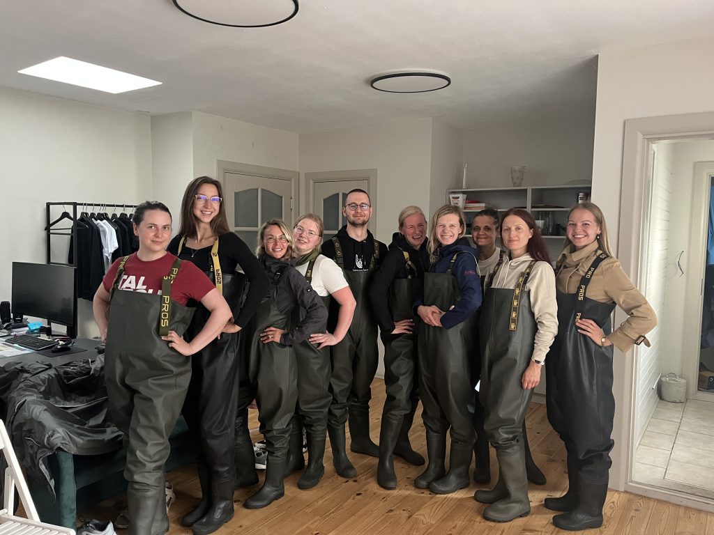 Group of individuals wearing waterproof waders, posing confidently in a bright indoor setting, showcasing teamwork and readiness for outdoor activities.