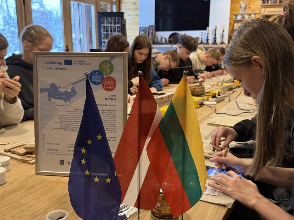 Group of people participating in a workshop with EU, Latvia, and Lithuania flags displayed, focusing on collaboration and cultural exchange.