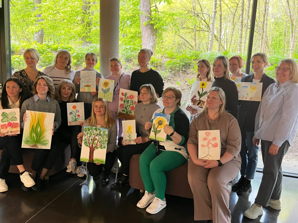 Group of individuals holding their artwork in a natural setting, showcasing a variety of colorful paintings and drawings during a creative workshop. Group of individuals holding their artwork in a natural setting, showcasing a variety of colorful paintings and drawings during a creative workshop.