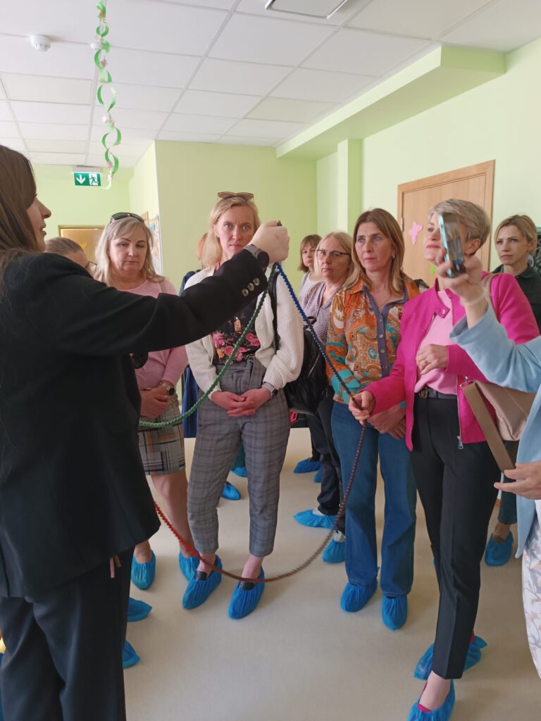 Group of women listening attentively to a speaker in a brightly lit room, wearing blue shoe covers, during a presentation or tour. Group of women listening attentively to a speaker in a brightly lit room, wearing blue shoe covers, during a presentation or tour.