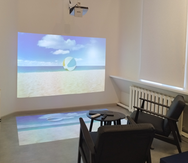 Therapeutic room featuring a beach-themed projection on a wall and floor, designed for innovative psychosocial and physical rehabilitation methods, promoting relaxation and social inclusion for vulnerable individuals. Therapeutic room featuring a beach-themed projection on a wall and floor, designed for innovative psychosocial and physical rehabilitation methods, promoting relaxation and social inclusion for vulnerable individuals.