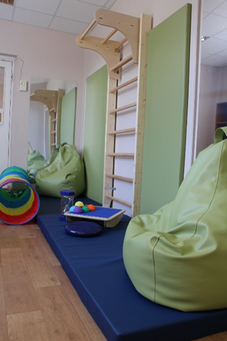 Rehabilitation therapy space featuring green bean bag chairs, a wooden climbing frame, and colorful sensory toys, designed for innovative psychosocial and physical rehabilitation methods for vulnerable individuals. Rehabilitation therapy space featuring green bean bag chairs, a wooden climbing frame, and colorful sensory toys, designed for innovative psychosocial and physical rehabilitation methods for vulnerable individuals.