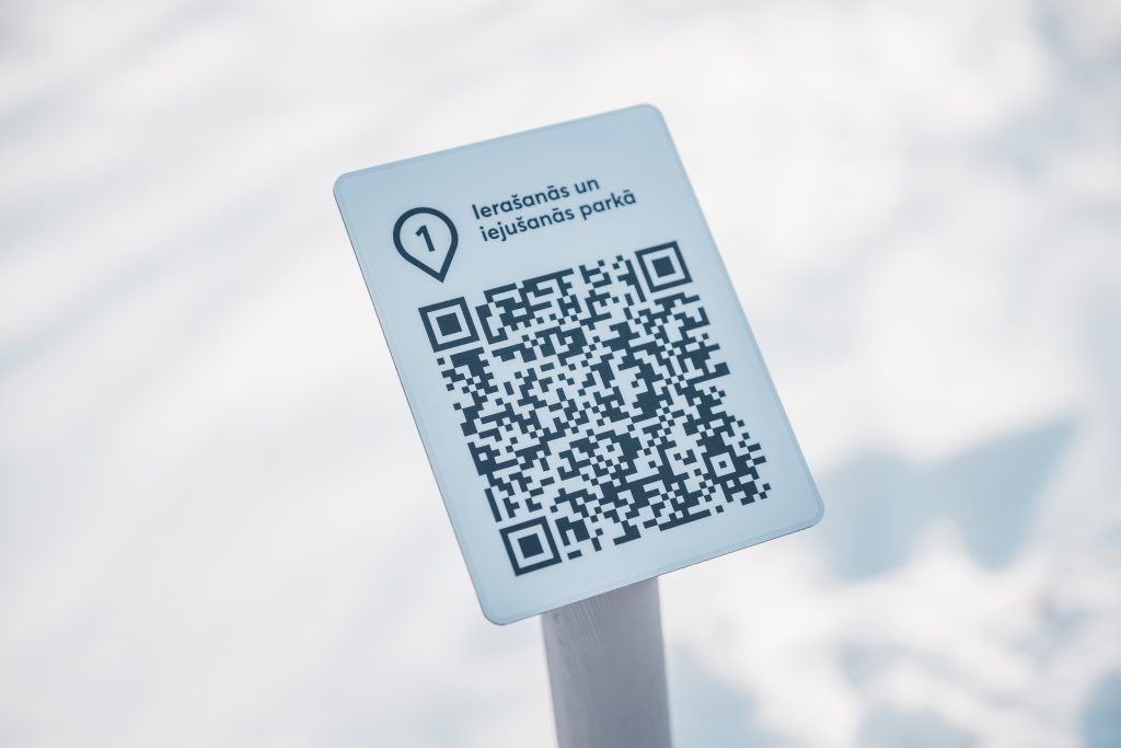 Sign displaying a QR code and location marker, indicating a point of interest related to psychosocial and physical rehabilitation methods for vulnerable individuals in a snowy environment. Sign displaying a QR code and location marker, indicating a point of interest related to psychosocial and physical rehabilitation methods for vulnerable individuals in a snowy environment.