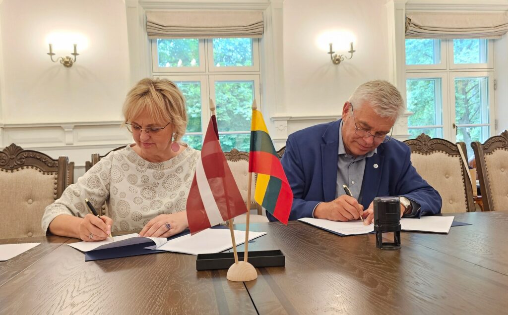 Representatives of project partners signing the documents, Latvia and Lithuania table flags on the table
