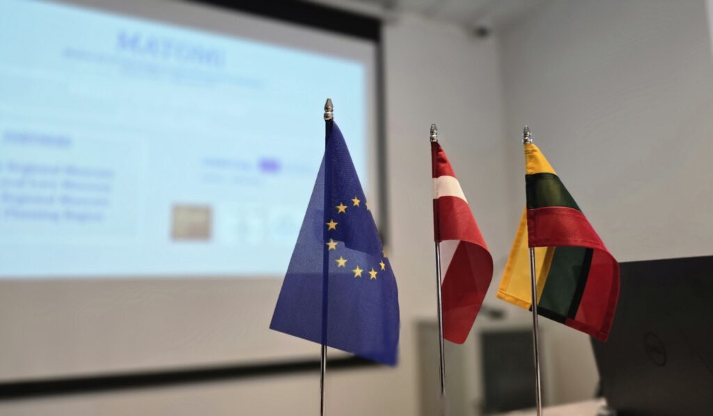 Photo of EU, LT and LV table flags, screen in the background