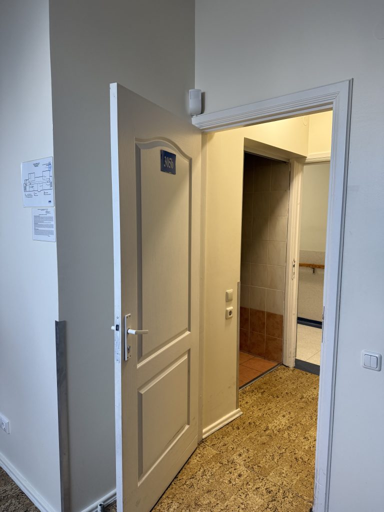 Interior view of a hallway with an open door leading to a small room, featuring neutral-colored walls and a tiled floor.