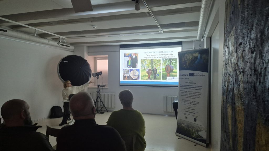 Audience attending a presentation in a well-lit room, featuring a screen displaying images and text, with a banner on the side promoting an event or organization. Audience attending a presentation in a well-lit room, featuring a screen displaying images and text, with a banner on the side promoting an event or organization.