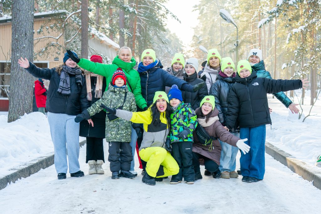 Group of people wearing bright green hats, enjoying a winter day outdoors in a snowy landscape, smiling and posing for the camera.