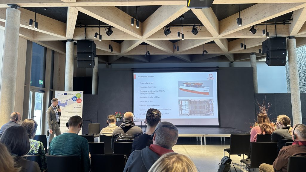 Audience attending a presentation in a modern conference room, featuring a projector screen displaying graphs and data. The setting includes wooden ceiling beams and a professional atmosphere. Audience attending a presentation in a modern conference room, featuring a projector screen displaying graphs and data. The setting includes wooden ceiling beams and a professional atmosphere.
