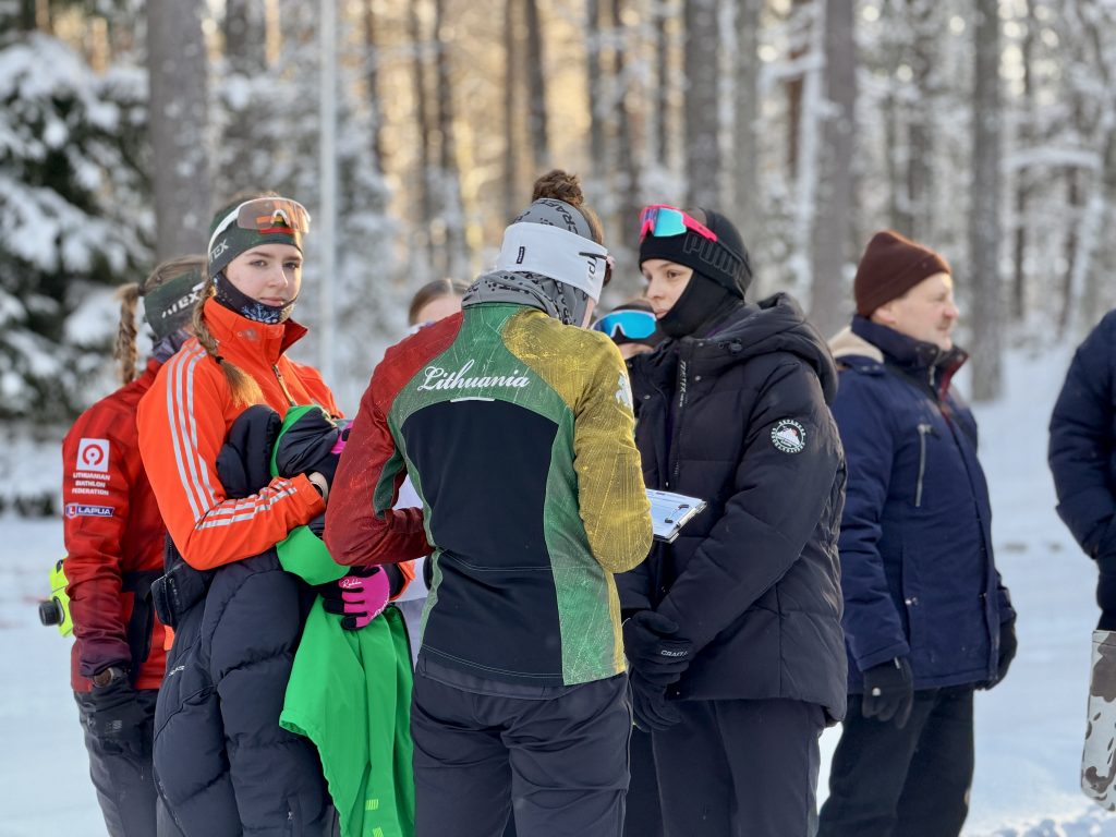 Group of athletes in winter sports attire discussing strategies outdoors in a snowy forest setting.