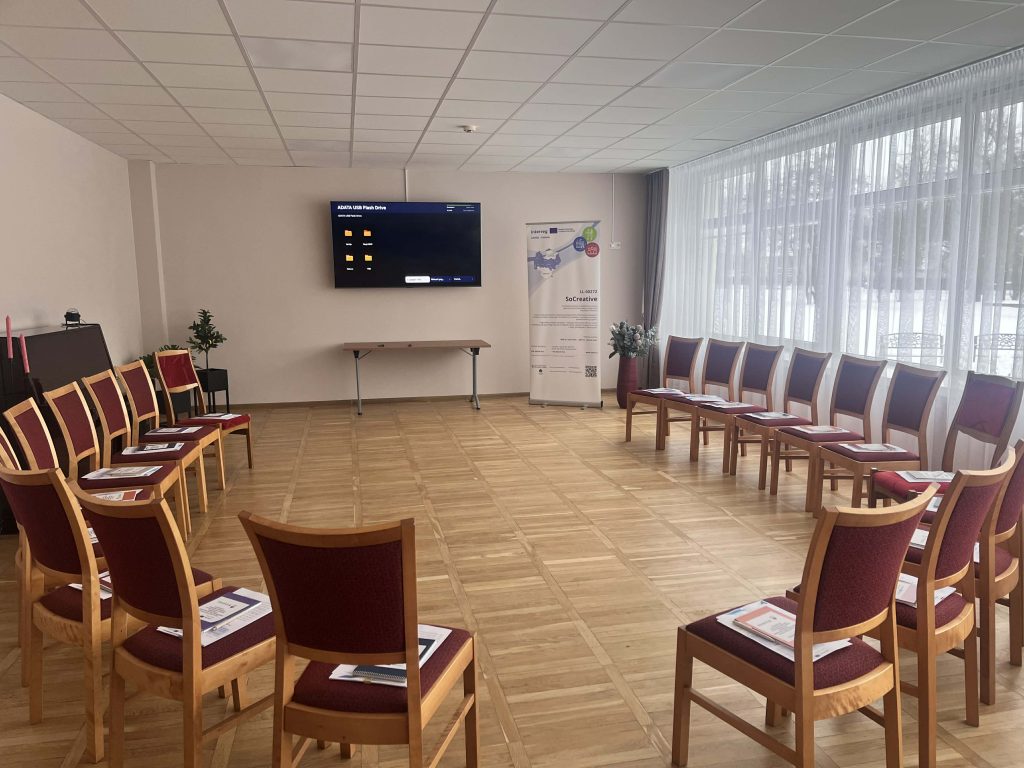 Modern meeting room setup featuring a circle of chairs, a wall-mounted TV for presentations, large windows providing natural light, and a welcoming atmosphere suitable for workshops or group discussions. Modern meeting room setup featuring a circle of chairs, a wall-mounted TV for presentations, large windows providing natural light, and a welcoming atmosphere suitable for workshops or group discussions.
