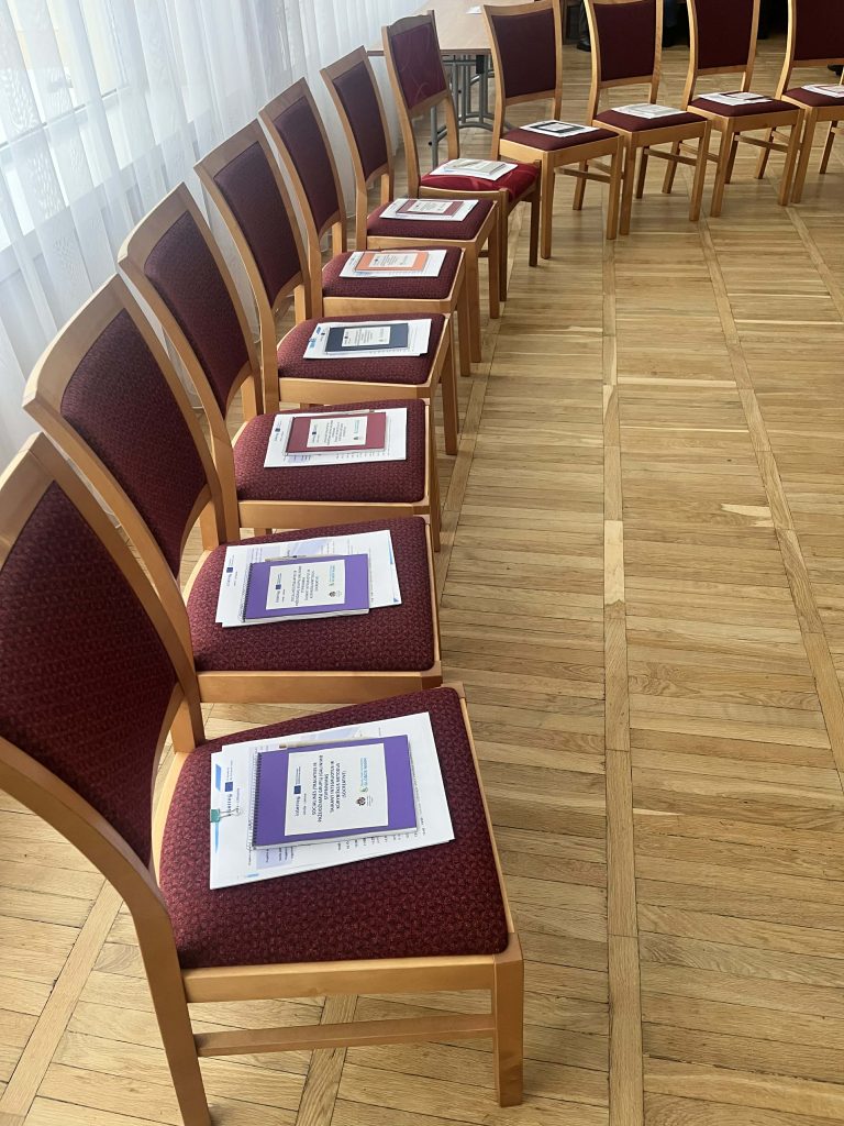 Row of wooden chairs with maroon upholstery, each featuring a folded document or program placed neatly on the seat, set in a well-lit room with wooden flooring. Row of wooden chairs with maroon upholstery, each featuring a folded document or program placed neatly on the seat, set in a well-lit room with wooden flooring.