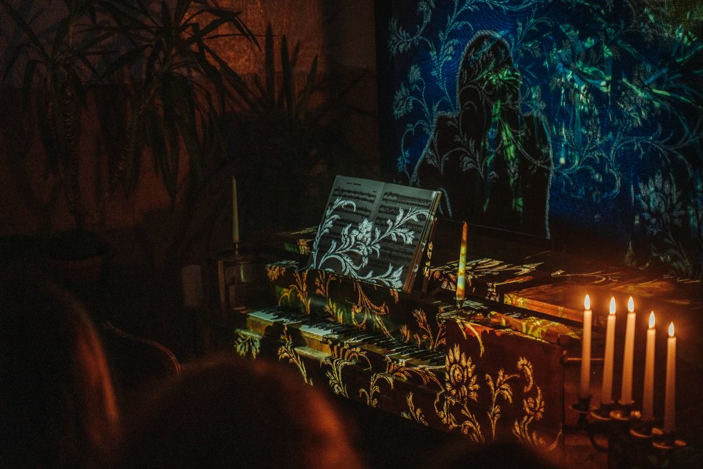 An altar setup featuring a dark, ornate tablecloth, candles, and an open book with intricate designs, illuminated by warm lighting. A colorful, mystical backdrop with abstract patterns and figures adds to the spiritual ambiance of the scene. An altar setup featuring a dark, ornate tablecloth, candles, and an open book with intricate designs, illuminated by warm lighting. A colorful, mystical backdrop with abstract patterns and figures adds to the spiritual ambiance of the scene.