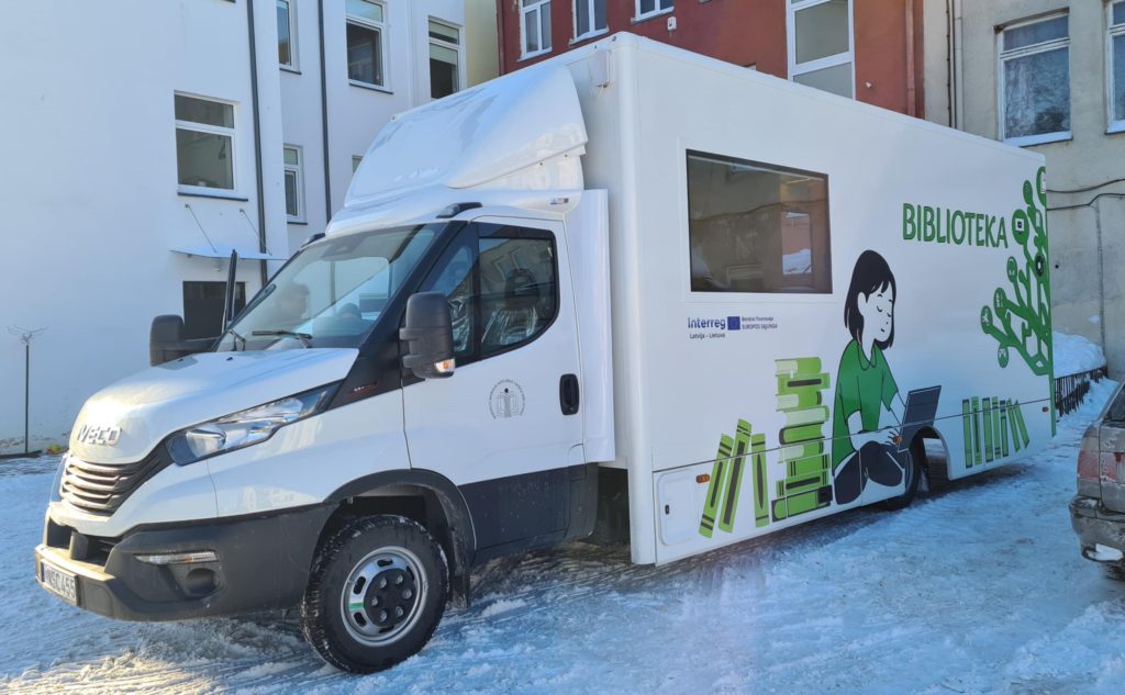 Mobile library truck parked on a snowy street, featuring a colorful graphic of a girl reading a book on its side.