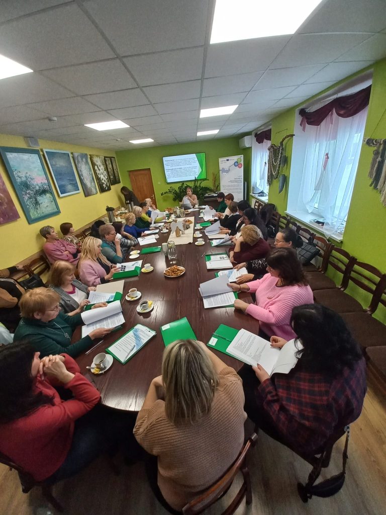 Group of professionals engaged in a collaborative meeting around a large table, with documents and laptops, in a brightly lit room featuring colorful artwork on the walls.