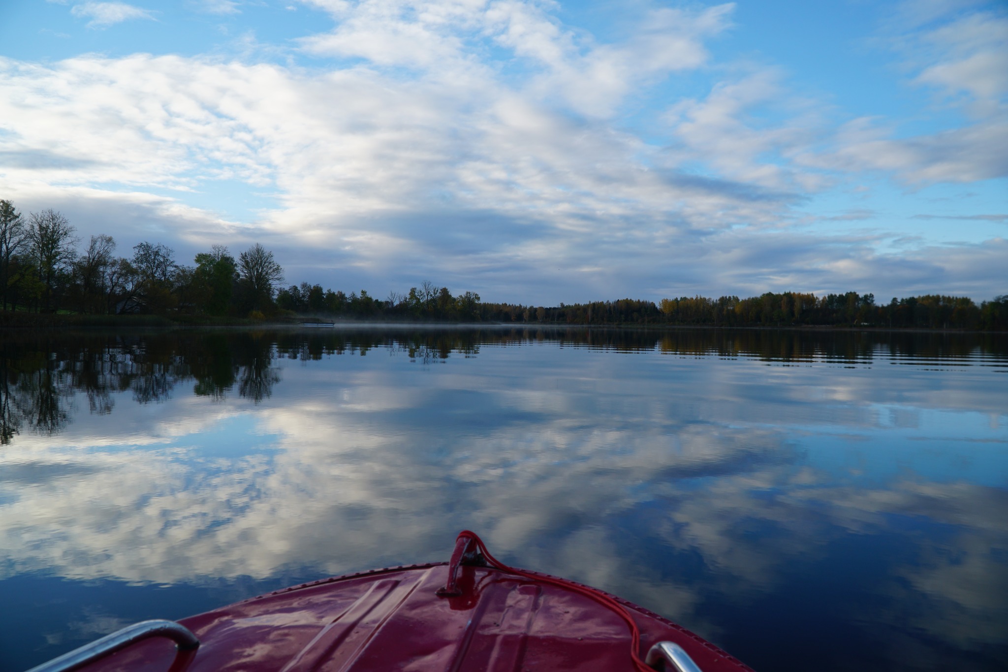 A serene view of a calm lake reflecting clouds and trees, with a red boat in the foreground. The scene captures the tranquility of nature and the beauty of a clear sky. A serene view of a calm lake reflecting clouds and trees, with a red boat in the foreground. The scene captures the tranquility of nature and the beauty of a clear sky.