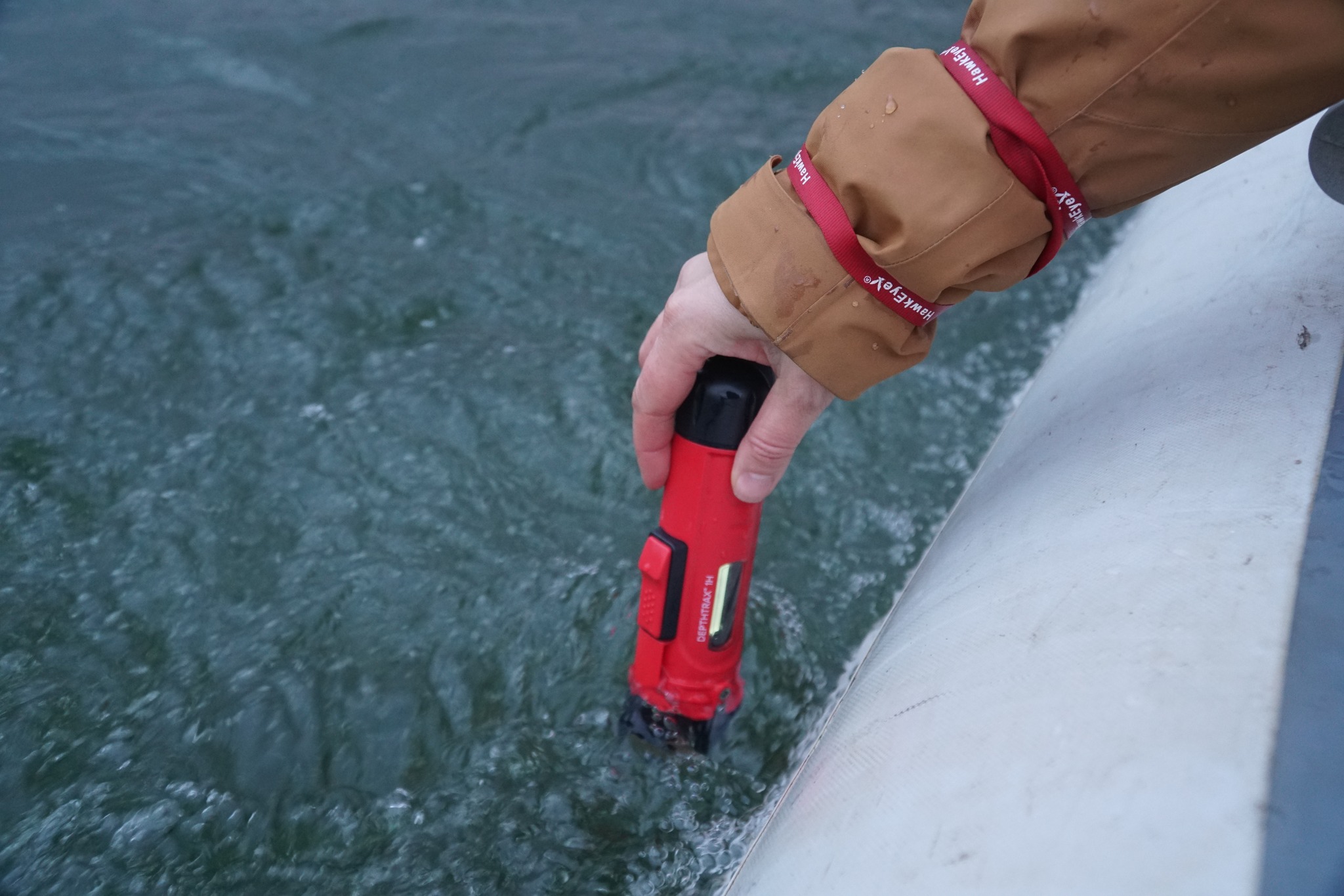 A person holding a red waterproof flashlight above water, demonstrating its functionality in a wet environment. A person holding a red waterproof flashlight above water, demonstrating its functionality in a wet environment.