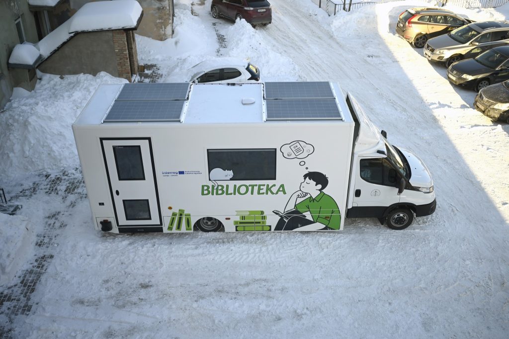 Mobile library truck parked in a snowy area, featuring a graphic of a person reading and the word "BIBLIOTEKA" prominently displayed on the side.