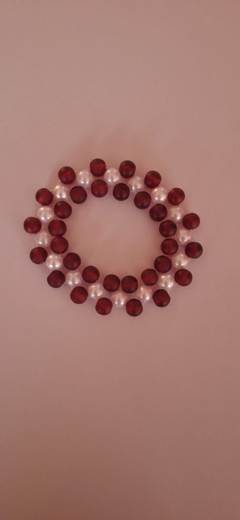 Elegant circular arrangement of maroon beads and white pearls on a soft pink background, showcasing a unique jewelry design.