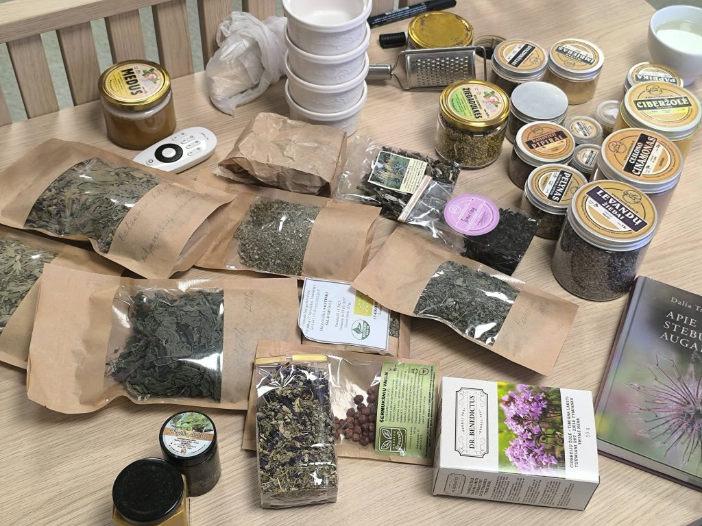 Assorted herbal teas and spices displayed on a wooden table, featuring various packaged herbs, jars, and a book about herbal remedies. The image showcases a collection of dried leaves, flowers, and spices, highlighting their diverse colors and textures.