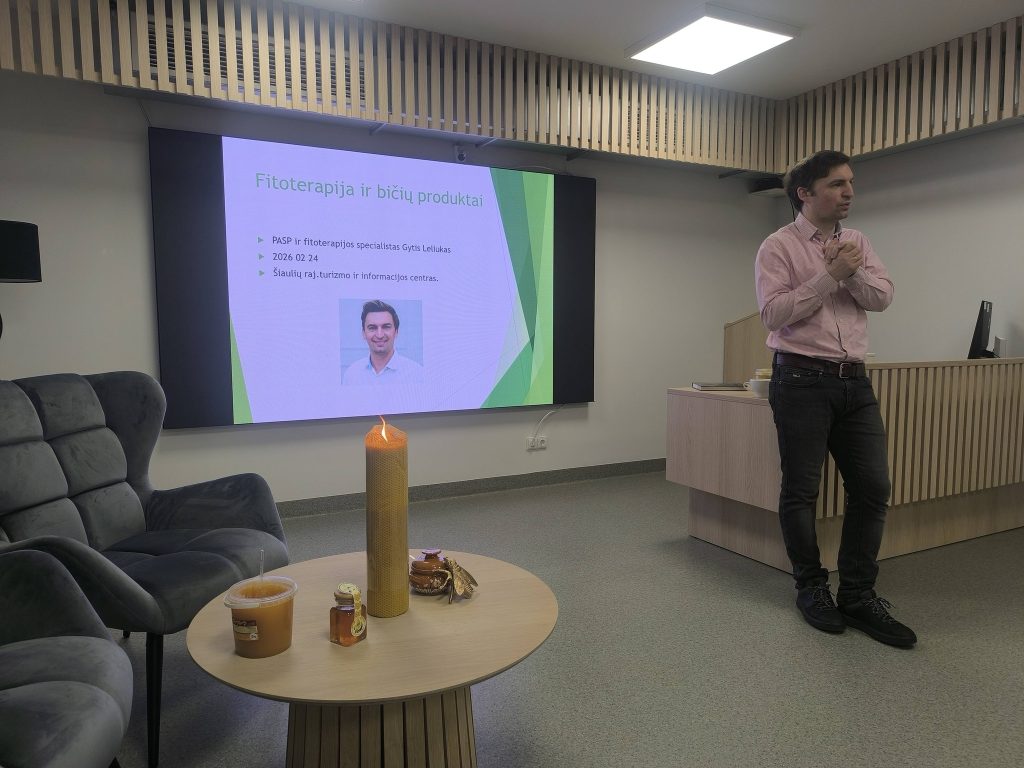 Presentation on herbal therapy and bee products by specialist Gytis Leliukas, featuring a candle and honey on a table, in a modern conference room setting.