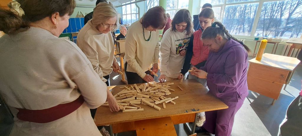 Group of people engaged in a collaborative activity using wooden sticks on a table in a bright classroom setting, promoting teamwork and creativity.