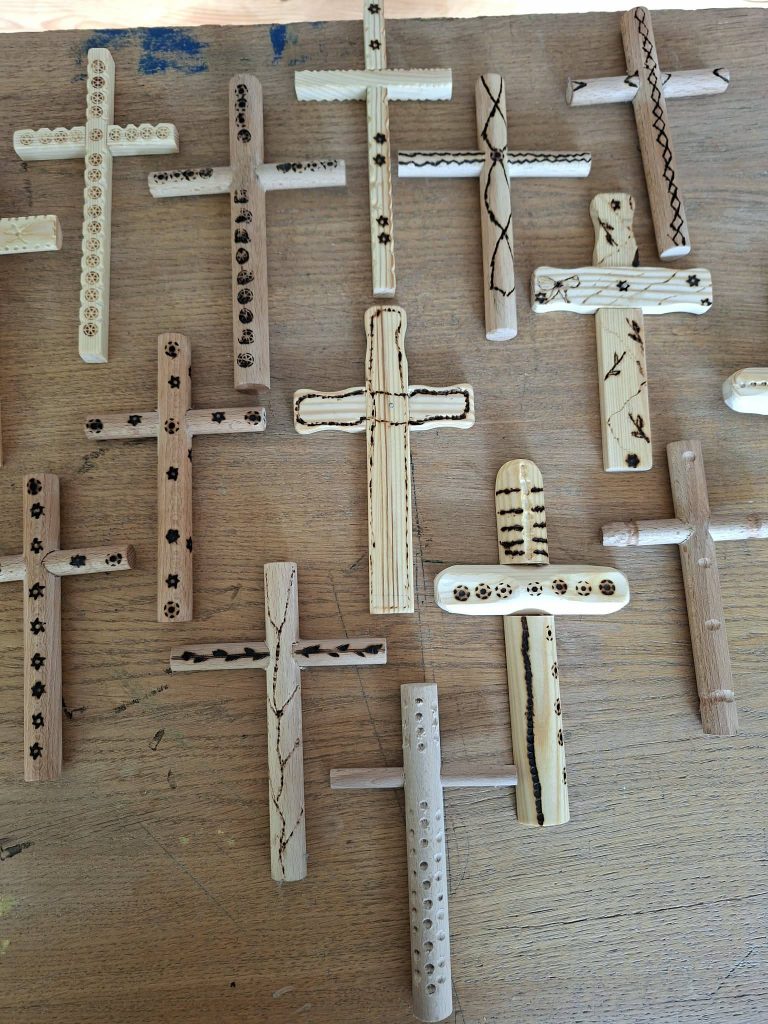 Handcrafted wooden crosses with intricate designs displayed on a wooden surface, showcasing various patterns and finishes. Ideal for religious decor or gift items.