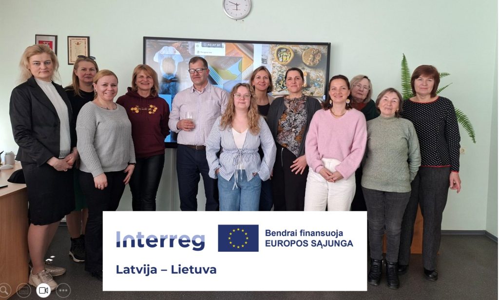 Group photo of participants from the Interreg Latvia-Lithuania project, showcasing collaboration and networking among professionals. The setting includes a presentation screen and features a diverse group of women and men engaged in discussions related to the project.