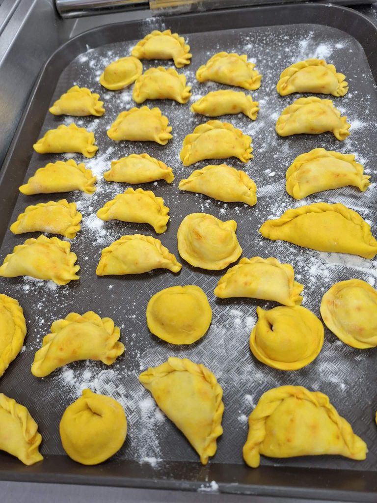Freshly made yellow dumplings arranged on a floured tray, showcasing various shapes and sizes, ready for cooking.