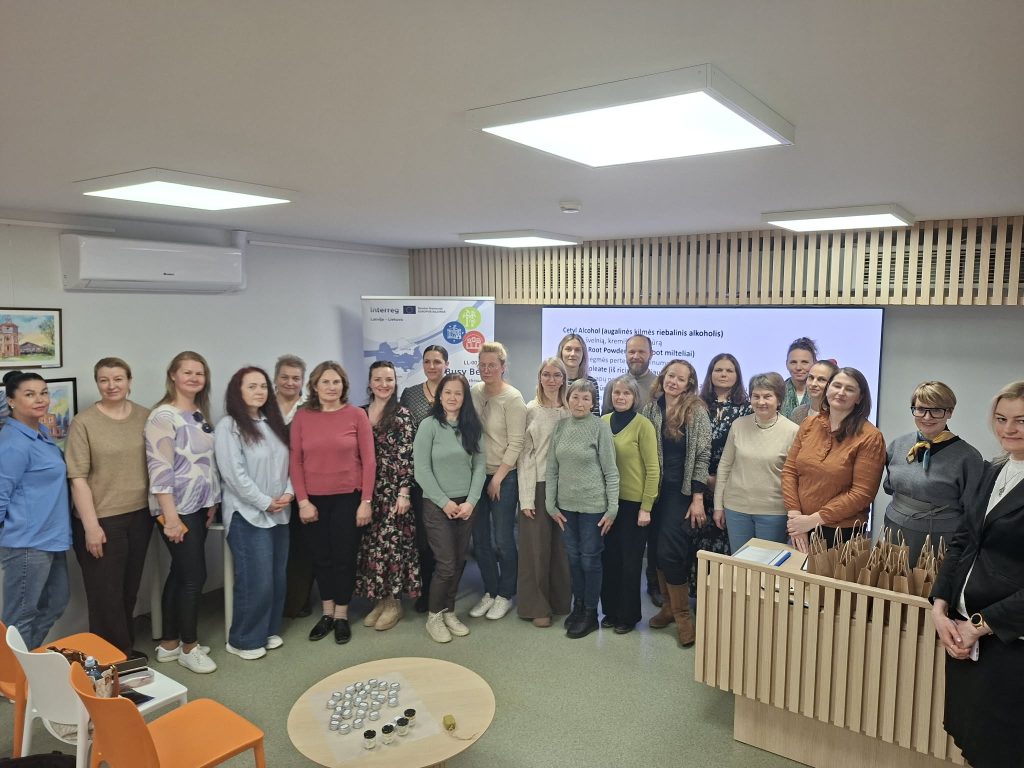 Group of participants at a workshop focused on community development and collaboration, featuring a diverse group of women standing together in a modern meeting space, with informational materials and a presentation screen in the background.