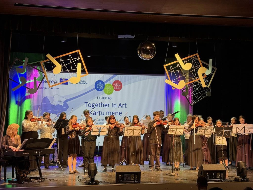A youth orchestra performance at the "Together In Art" event in Latvia, showcasing musicians playing violins and piano on stage, with colorful lighting and musical notes decor in the background.
