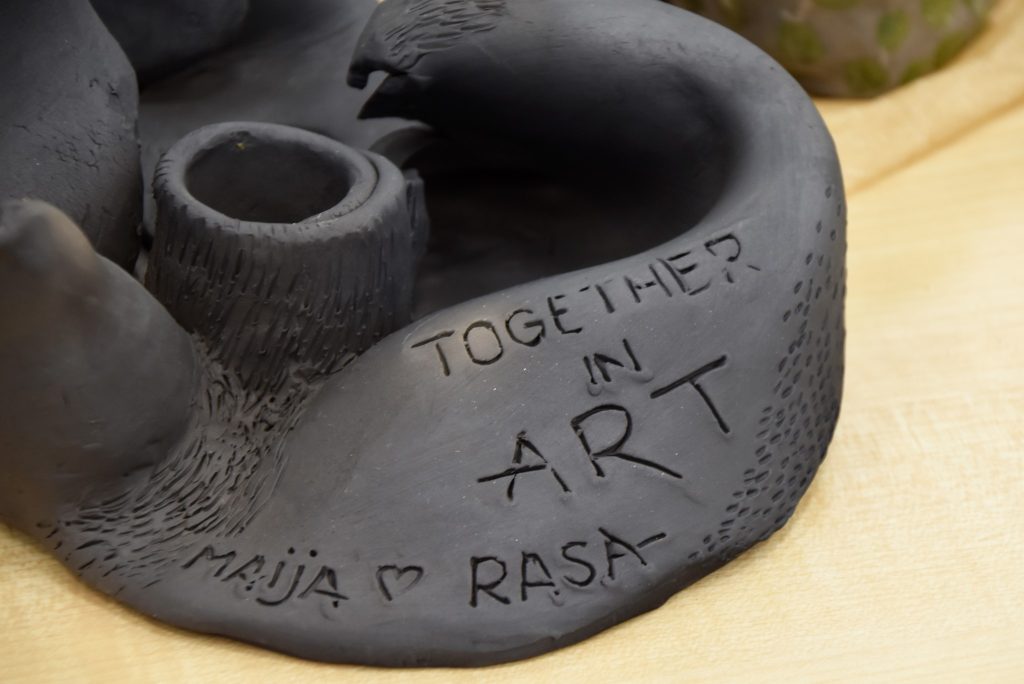 Ceramic artwork featuring a textured black surface with engraved text that reads "Together in Art" and names "Maja" and "Rasa," showcasing a collaborative artistic expression.