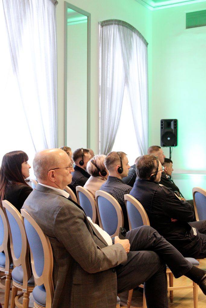 Audience members wearing headsets attentively listen during a conference in a well-lit room with large windows and elegant decor.