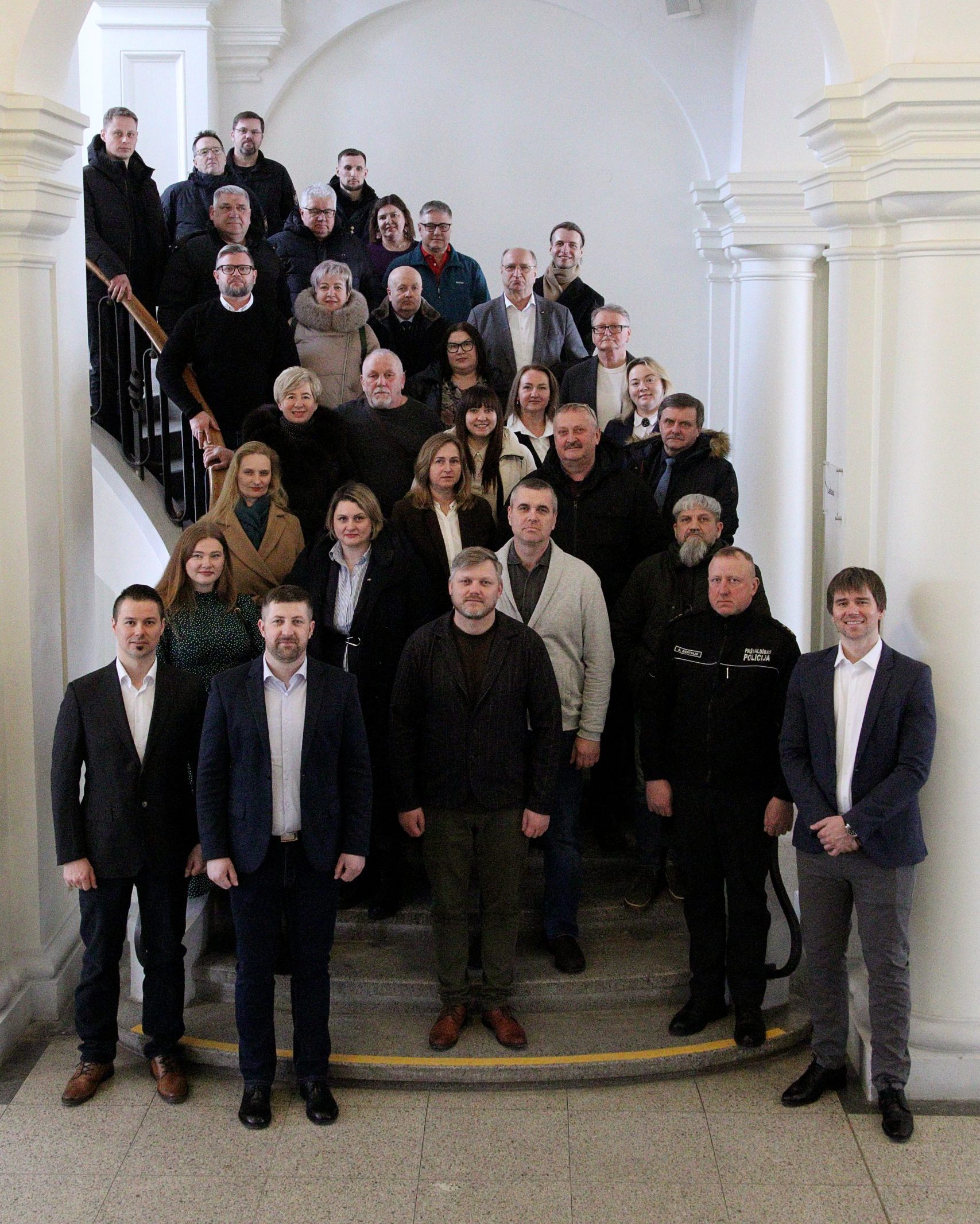 Group photo of diverse individuals gathered on a staircase in a well-lit, elegant building, showcasing a blend of professional attire and casual wear, indicating a collaborative or community event.