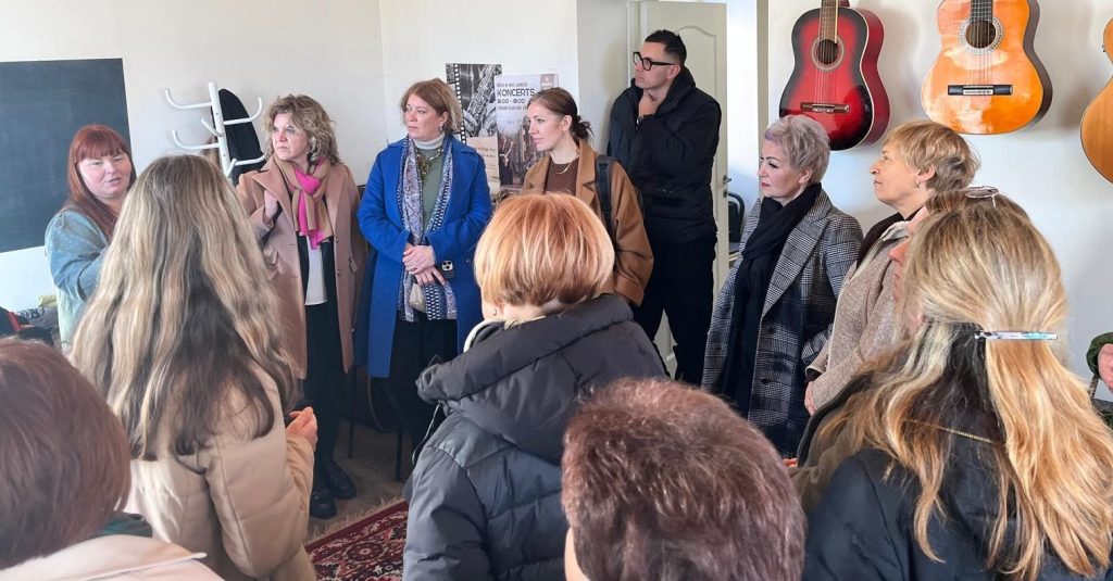 Group of women engaged in a discussion during a workshop in a cozy room decorated with guitars. The setting features a chalkboard and a warm atmosphere, highlighting collaboration and community learning.