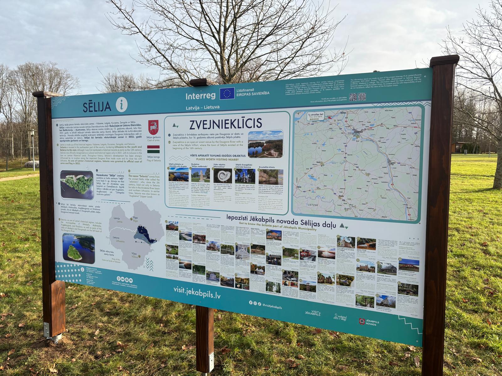 Informative sign about the Selija region in Latvia, featuring maps, local attractions, and cultural information. The sign is located in a park setting with trees in the background.