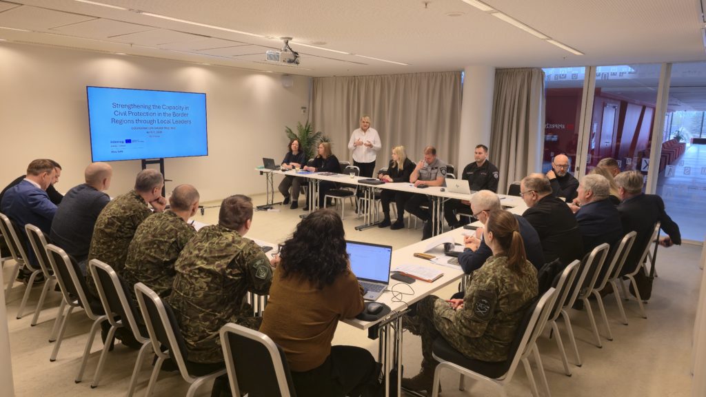 Meeting of civil protection officials discussing strategies to enhance local capacity in border regions, with a presentation on screen and participants engaged at a conference table. Meeting of civil protection officials discussing strategies to enhance local capacity in border regions, with a presentation on screen and participants engaged at a conference table.