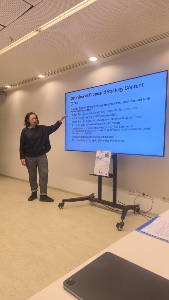 Woman presenting an overview of a proposed strategy for enhancing emergency preparedness and civil protection capabilities, with a focus on border security, military threats, and cyber risks, in a conference room setting. Woman presenting an overview of a proposed strategy for enhancing emergency preparedness and civil protection capabilities, with a focus on border security, military threats, and cyber risks, in a conference room setting.