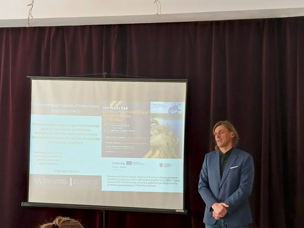 Image of a seminar presentation at Vidzeme University of Applied Sciences, featuring a speaker discussing water tourism development in the Vidzeme region. The presentation slide highlights resources and socio-economic assessments related to sustainable tourism. The setting includes a dark curtain backdrop, and the speaker is dressed in a formal outfit. Image of a seminar presentation at Vidzeme University of Applied Sciences, featuring a speaker discussing water tourism development in the Vidzeme region. The presentation slide highlights resources and socio-economic assessments related to sustainable tourism. The setting includes a dark curtain backdrop, and the speaker is dressed in a formal outfit.
