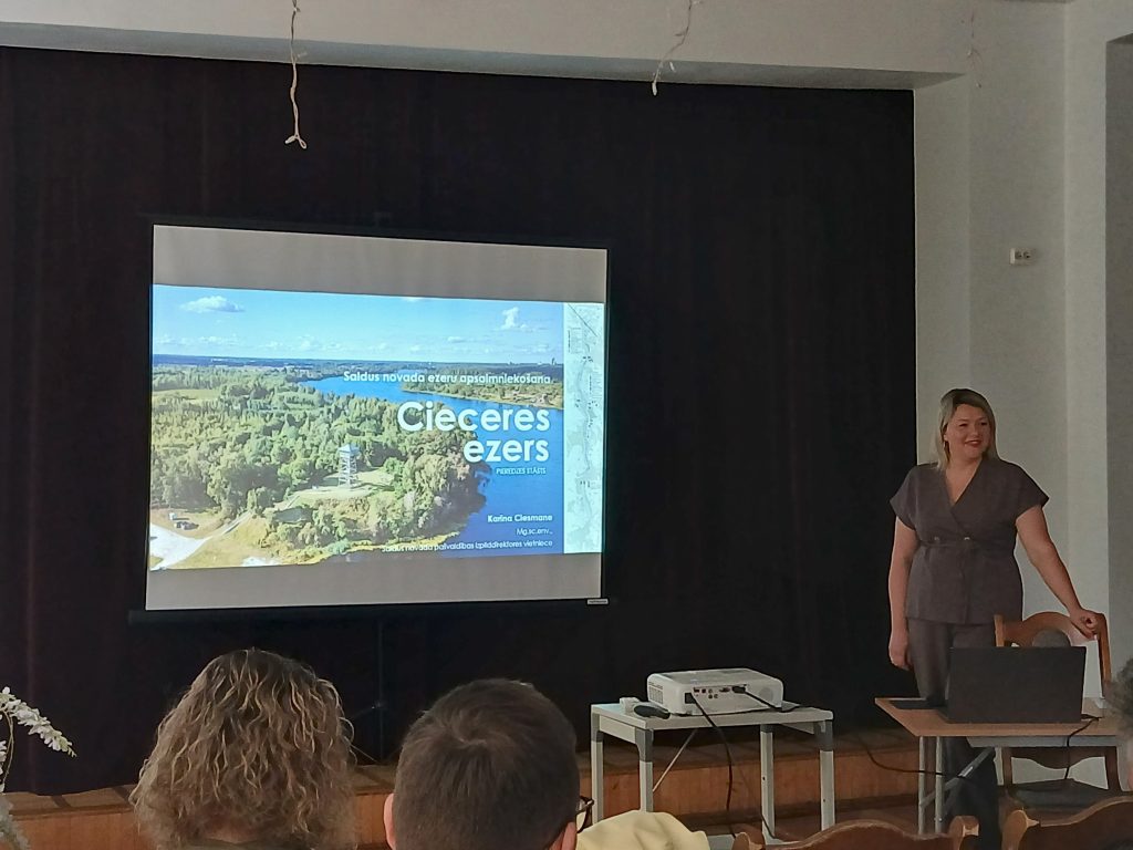Presentation on Ciecere Lake tourism by Karina Clesmane, featuring a scenic view of the lake and surrounding nature, with a projector displaying information about local attractions and activities. Presentation on Ciecere Lake tourism by Karina Clesmane, featuring a scenic view of the lake and surrounding nature, with a projector displaying information about local attractions and activities.