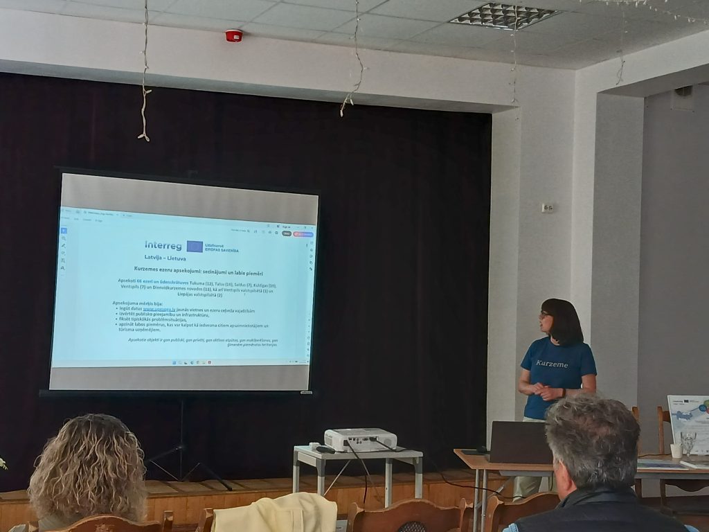 Presenter discussing a project related to Latvia and Lithuania at a seminar, with a projector screen displaying information about the initiative. The setting includes an audience engaged in the presentation. Presenter discussing a project related to Latvia and Lithuania at a seminar, with a projector screen displaying information about the initiative. The setting includes an audience engaged in the presentation.