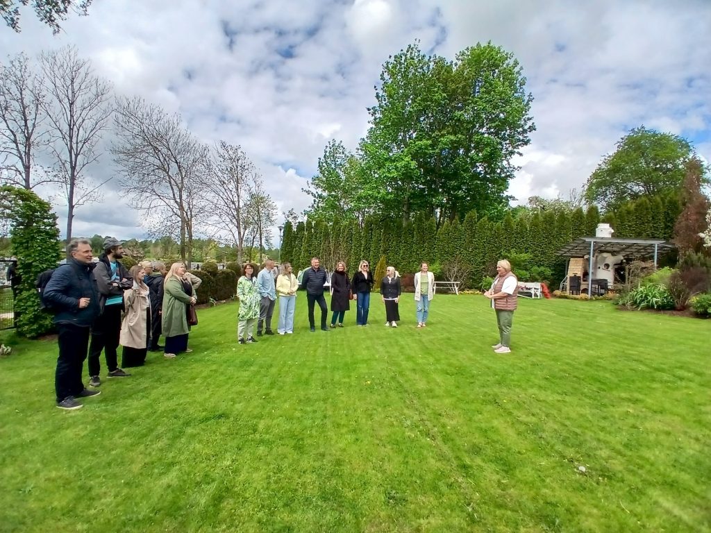 Group of people gathered in a lush green garden, listening attentively to a speaker. The scene captures a social or community event with trees and a cozy outdoor setting in the background. Group of people gathered in a lush green garden, listening attentively to a speaker. The scene captures a social or community event with trees and a cozy outdoor setting in the background.
