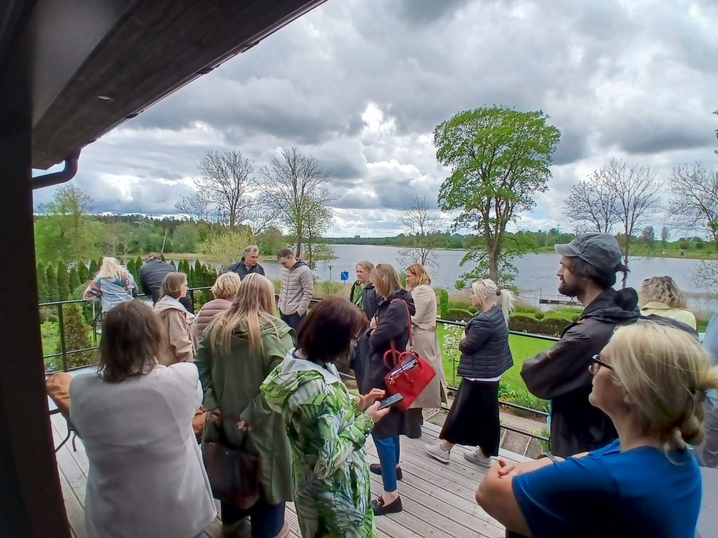 Group of people gathered on a wooden deck overlooking a scenic lake, with cloudy skies and greenery in the background, during a social event or gathering. Group of people gathered on a wooden deck overlooking a scenic lake, with cloudy skies and greenery in the background, during a social event or gathering.