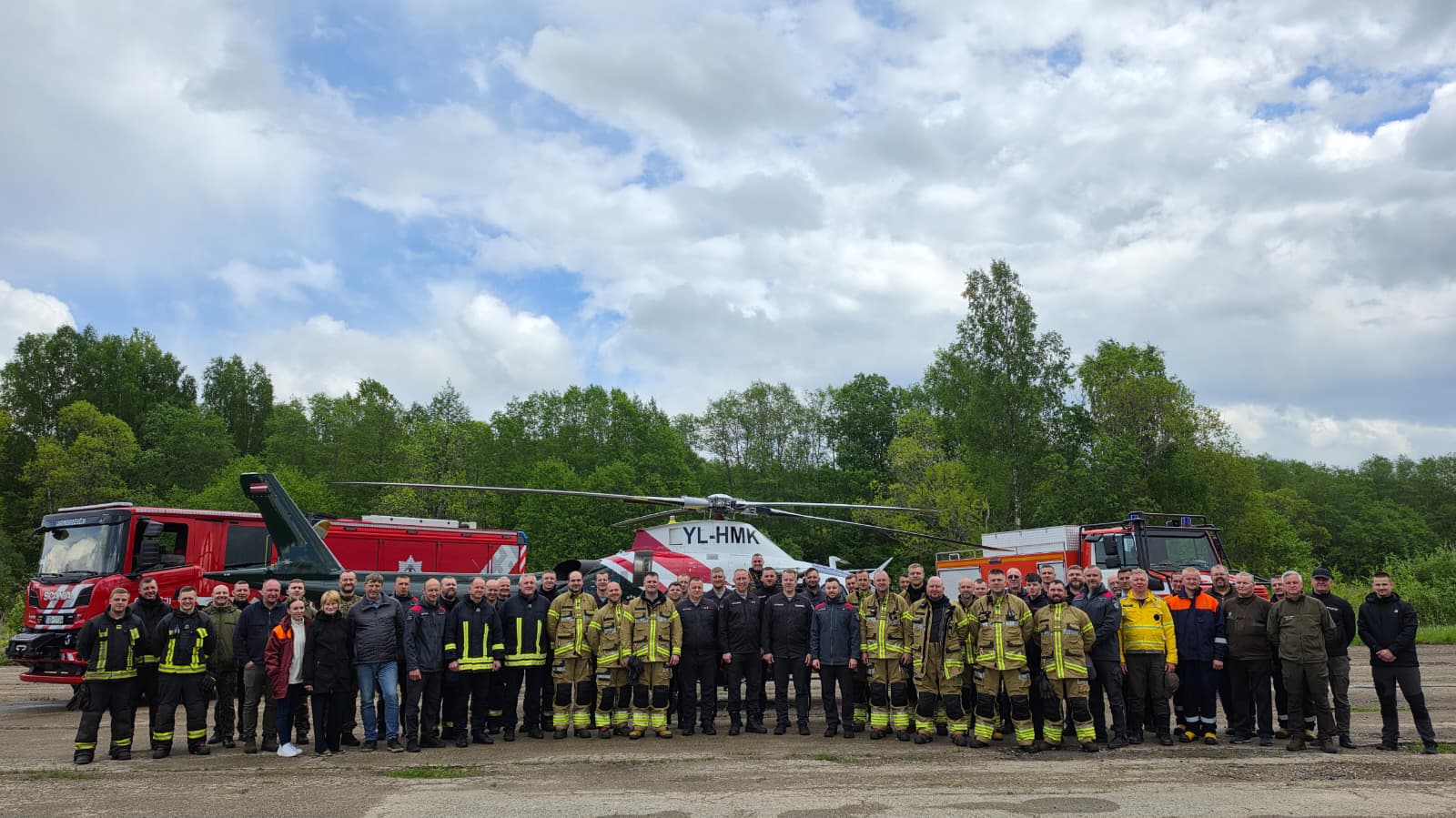Group photo of firefighters, emergency responders, and support personnel standing in front of fire trucks and a helicopter, showcasing teamwork and readiness for emergency services.
