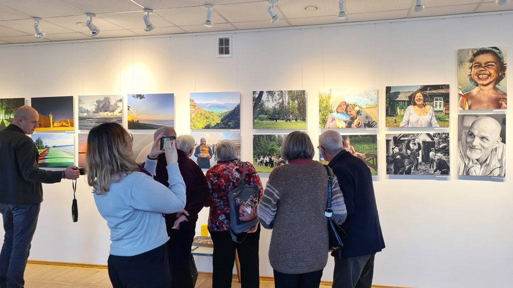 A group of visitors admiring a photography exhibition featuring various images on the wall, showcasing landscapes and portraits, in a well-lit gallery space. A group of visitors admiring a photography exhibition featuring various images on the wall, showcasing landscapes and portraits, in a well-lit gallery space.