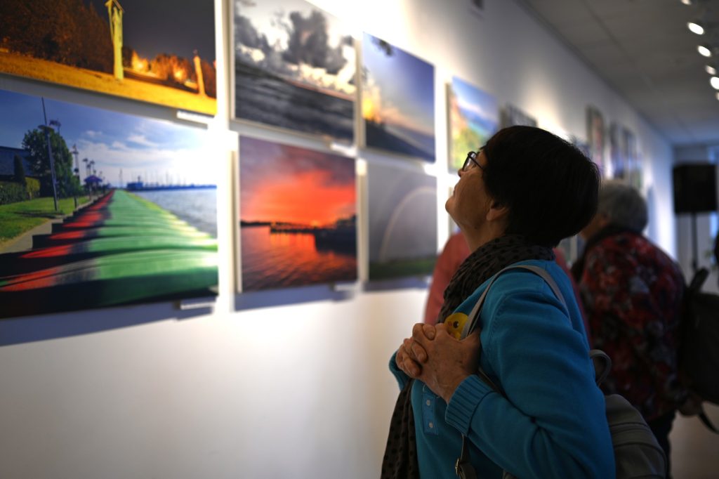 Woman admiring a gallery of landscape photographs on display, showcasing vibrant colors and serene scenes, in an art exhibition setting. Woman admiring a gallery of landscape photographs on display, showcasing vibrant colors and serene scenes, in an art exhibition setting.