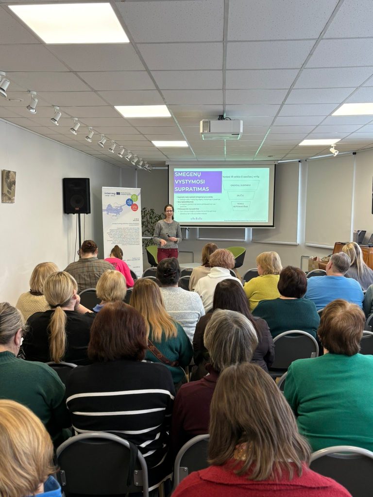 A speaker presents to an engaged audience during a seminar on brain development and understanding, with a projector displaying key points in the background. The attendees, mostly women, are seated and focused on the presentation in a well-lit conference room. A speaker presents to an engaged audience during a seminar on brain development and understanding, with a projector displaying key points in the background. The attendees, mostly women, are seated and focused on the presentation in a well-lit conference room.