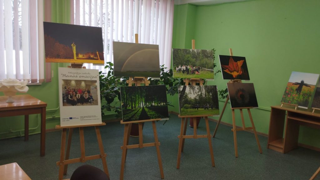 Photographic exhibition titled "Manas emocijas" featuring various nature and community-themed images displayed on easels in a green room. The exhibit showcases vibrant photographs, including landscapes and group activities, highlighting emotional connections to nature. Photographic exhibition titled "Manas emocijas" featuring various nature and community-themed images displayed on easels in a green room. The exhibit showcases vibrant photographs, including landscapes and group activities, highlighting emotional connections to nature.